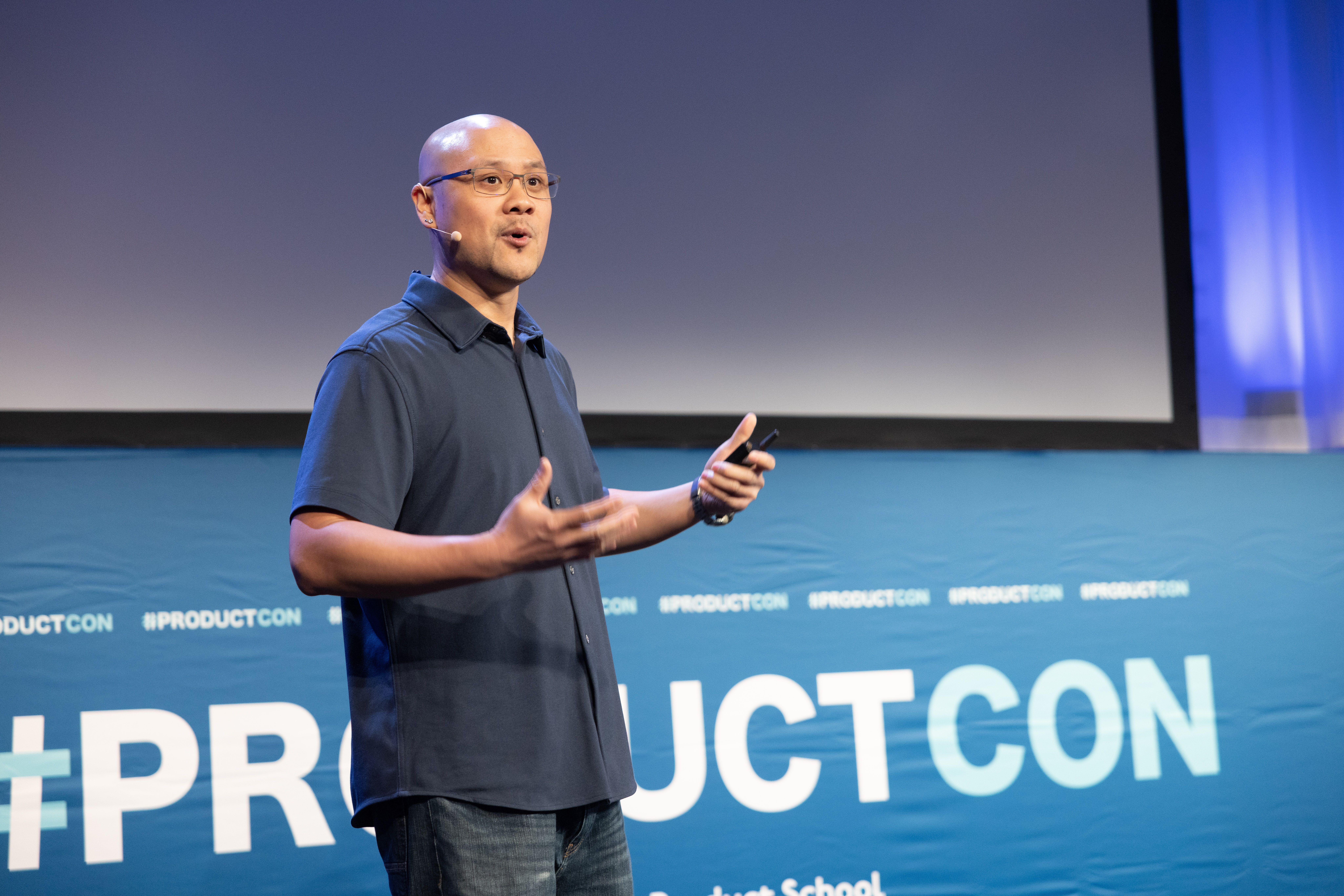 Chino presenting at ProductCon on stage with presentation slides behind him, discussing design leadership and product development strategies
